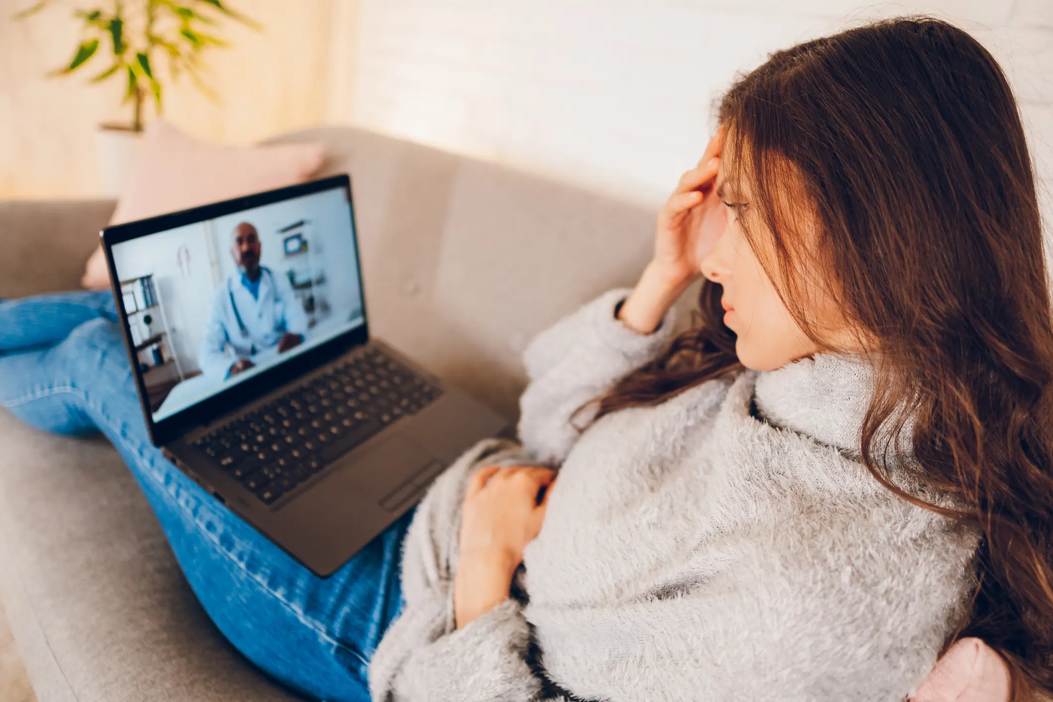 Woman reclining on a couch with a laptop on her lap participating in a telehealth video session with a clinician, suggesting remote counseling and therapy options for new and current patients