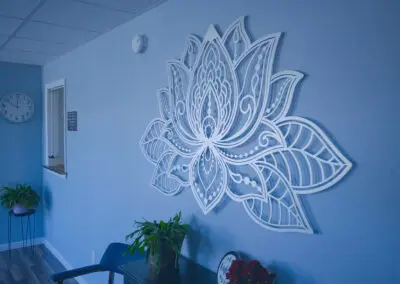 Reception area with blue walls featuring a large white decorative lotus wall art above a black table holding potted plants and a small sign, a clock and service window to the left